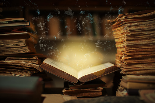 Magical book lying open on desk in library. Fairies from fairy tale flying from glowing pages and illuminates surrounding.